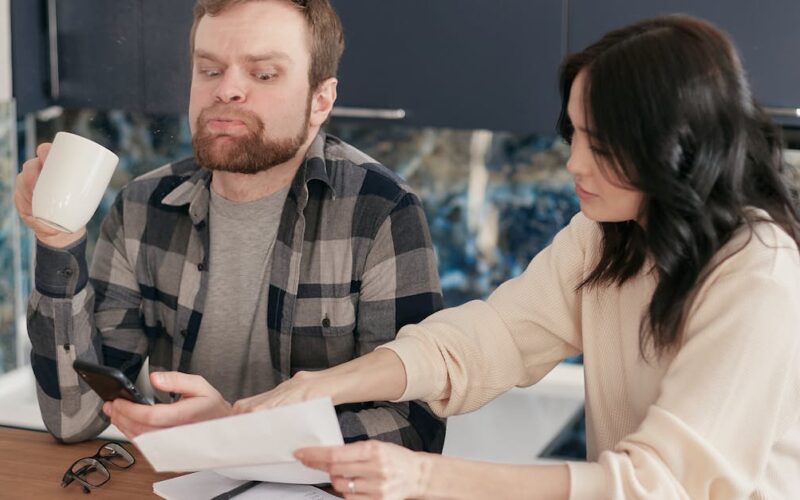restituição imposto de renda falecido — A couple looks worried as they review bills at their kitchen table, reflecting financial concerns.