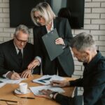 regime fiscal das LLCs — Three mature professionals in a business meeting discussing and signing documents in an office setting.
