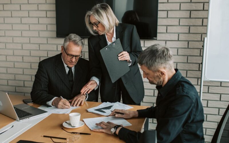 regime fiscal das LLCs — Three mature professionals in a business meeting discussing and signing documents in an office setting.