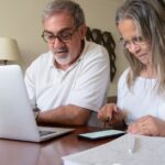 previdência complementar — Senior couple working together on documents with laptop and phone at home.