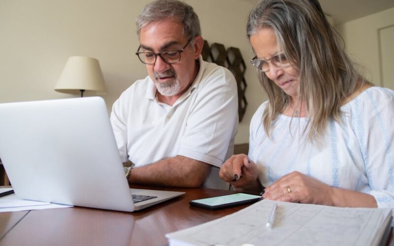 previdência complementar — Senior couple working together on documents with laptop and phone at home.