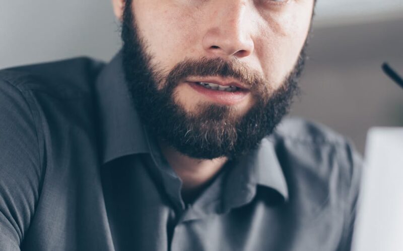 desaparecimento forçado e tortura — Worried man with beard reviewing financial paperwork indoors, holding cup.