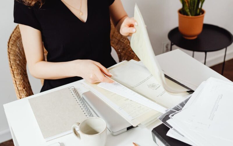 organização documentos pessoais — Woman sorting through documents in a home office setting. Organized workspace with plants.