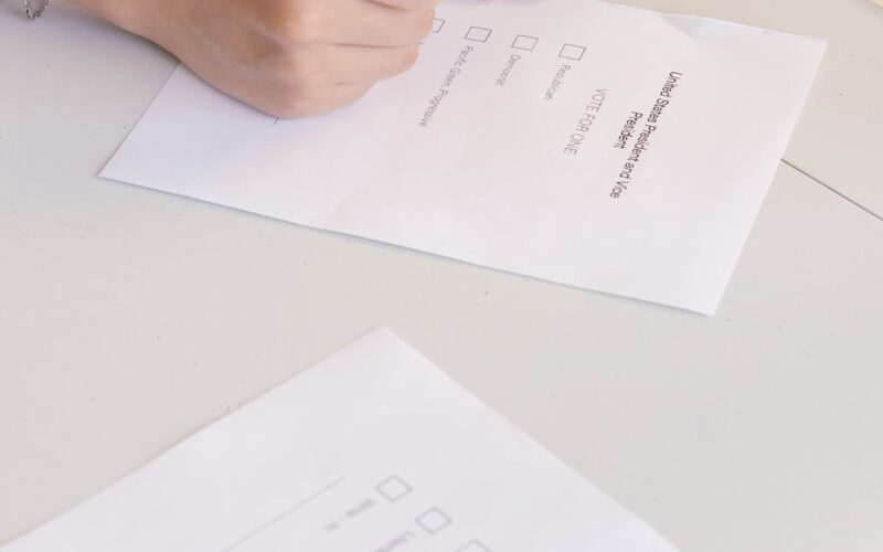 pesquisa eleitoral brasileira — An individual is marking a ballot paper at an election booth, symbolizing democratic participation.