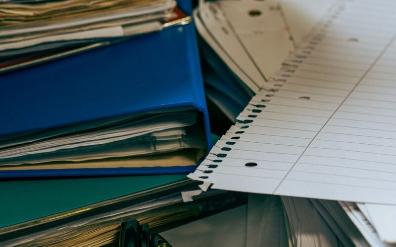 organizar documentos pessoais — A neat and organized desk featuring stacks of paper, folders, pens, and a computer mouse.
