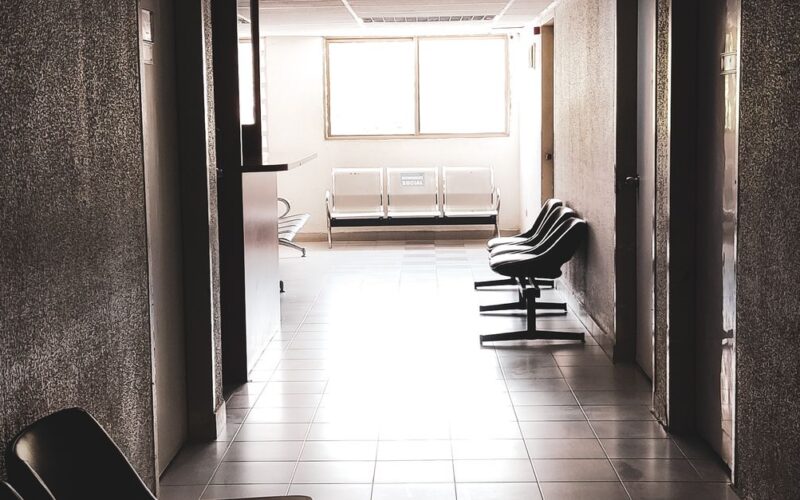 filas cirurgias ortopédicas público — A dimly lit empty corridor with chairs and a waiting area, conveying a quiet atmosphere.
