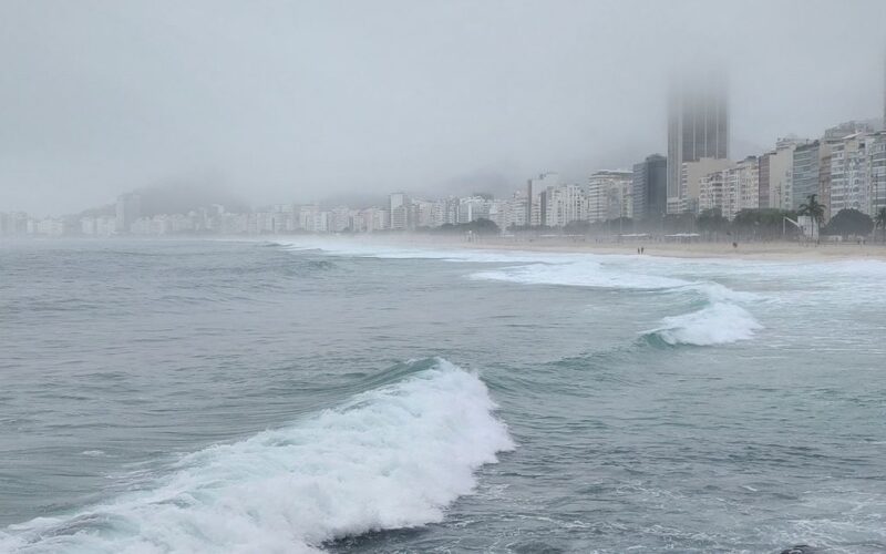 frio rigoroso no Sul do Brasil — A foggy view of the ocean with city skyline in the mist, rocky shoreline front.
