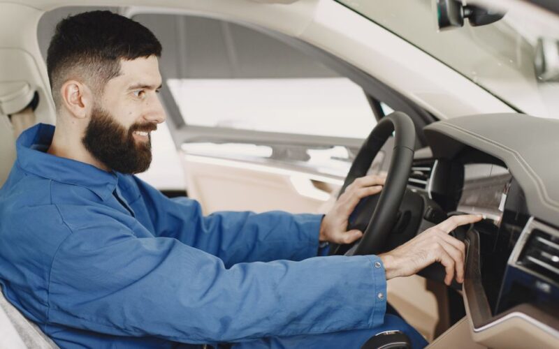 escolher carro ideal — Mechanic in blue coveralls interacts with car dashboard, smiling and focused.