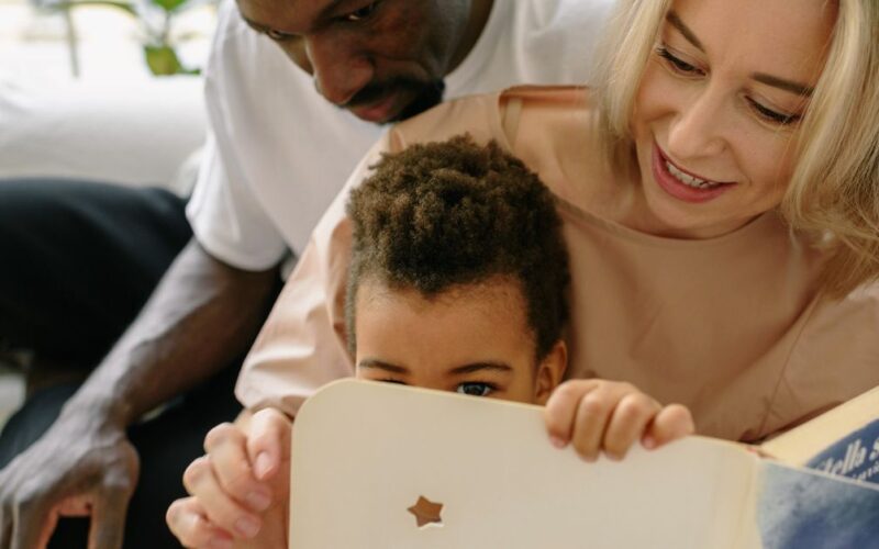 família de acolhimento — Interracial family enjoying quality time reading a book indoors together.
