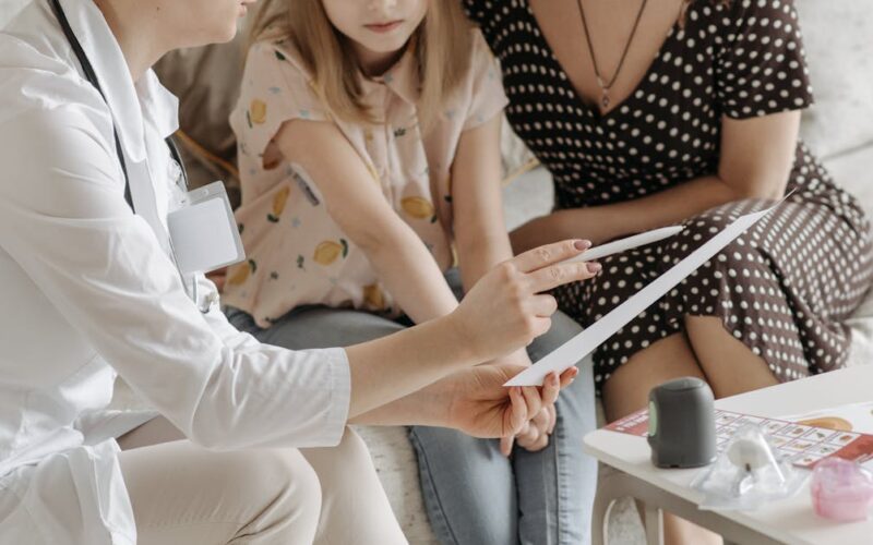 família de acolhimento — Doctor discussing health care plan with mother and daughter on sofa.