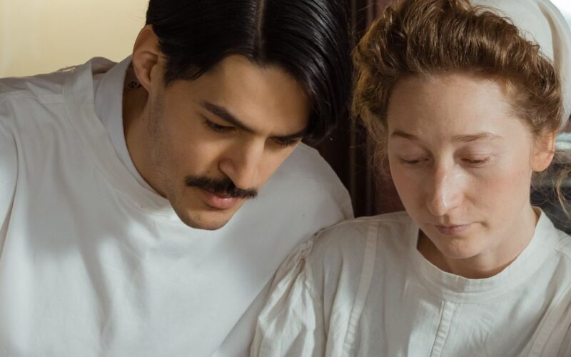 escolher curso de medicina — Two pharmacists in vintage attire examining medical books in a classic pharmacy setting.