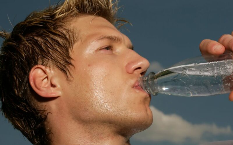 ondas de calor na Europa — Close-up of a sweaty athletic man drinking water outdoors to cool off and stay hydrated.