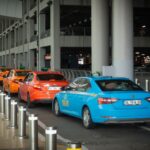regras tarifas serviços táxi — Vibrant taxis lined up at Istanbul Airport arrival terminal with passengers and drivers interacting.