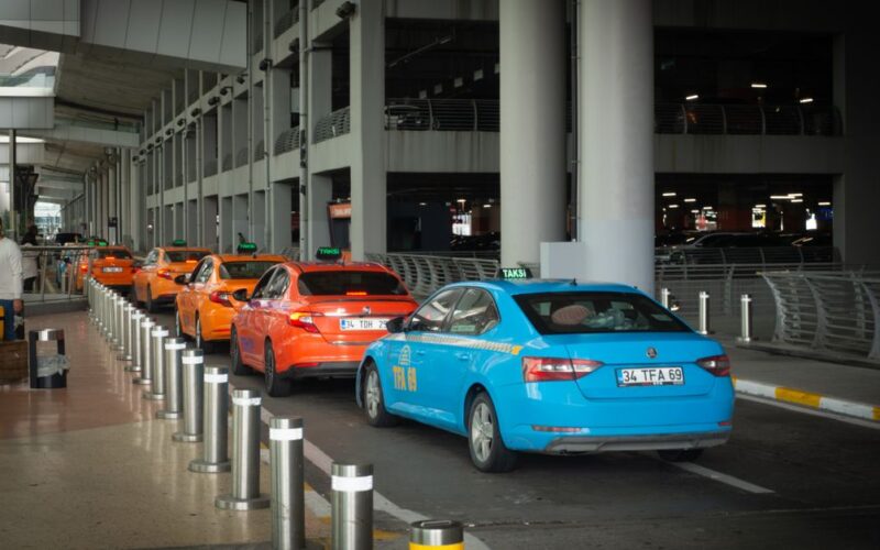 regras tarifas serviços táxi — Vibrant taxis lined up at Istanbul Airport arrival terminal with passengers and drivers interacting.