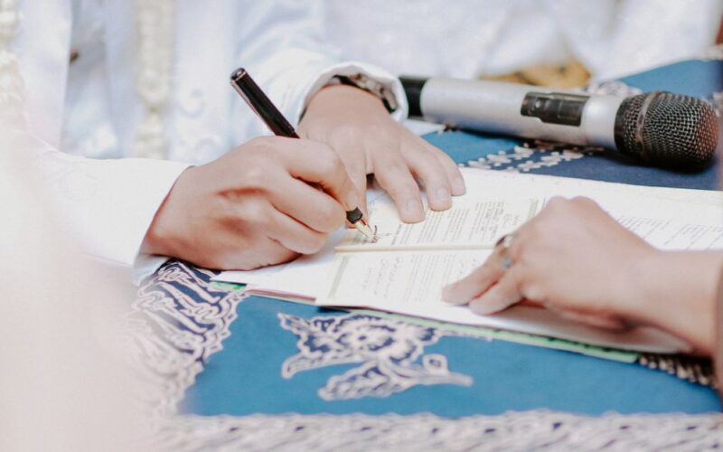 planejar testamento — Close-up of hands signing wedding documents with microphone on table.