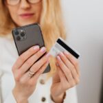 segurança financeira com Pix — A woman holding a smartphone and credit card, engaging in online shopping indoors.