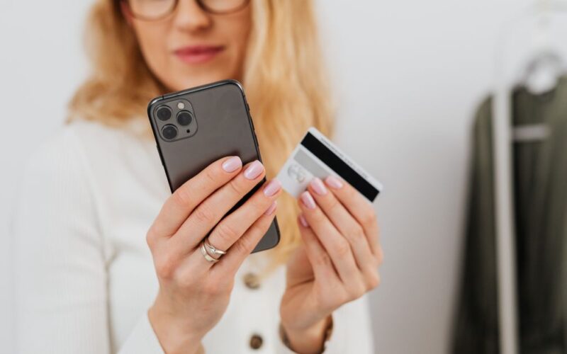 segurança financeira com Pix — A woman holding a smartphone and credit card, engaging in online shopping indoors.