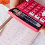 orçamento familiar — Hands using a red calculator surrounded by financial documents and receipts, symbolizing financial management.