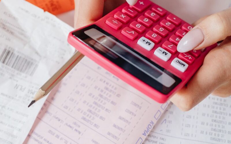 orçamento familiar — Hands using a red calculator surrounded by financial documents and receipts, symbolizing financial management.