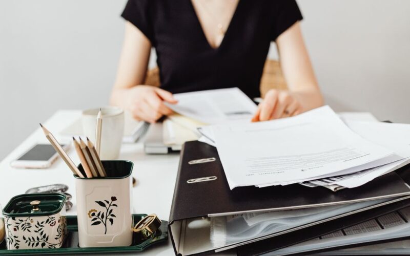 organizar documentos pessoais — A woman at a desk working with binders and documents, featuring essential office supplies.